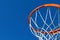 Detail of an orange basketball rim hoop and white net against blue sky