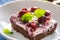 Detail of a piece of brownie with a cream, cherries and fresh mint leaves on a plate