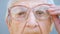 Detail portrait of granny in eyeglasses with pensive sight. Close up wrinkled face of female pensioner looking into