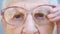 Detail portrait of granny in eyeglasses with pensive sight. Close up wrinkled face of female pensioner looking into