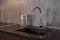 Detail of a rectangular designer kitchen sink with chrome water tap against a gray textured wall.