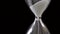 Detail of sand pouring in hourglass on black background, time passing concept