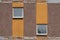 Detail of a shabby prefabricated concrete house brown wall with two decorative windows and vertical orange lines, close-up,