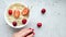 Detail shot of a kitchen table with a white cup of oatmeal and strawberries and a hand that lays strawberries on the