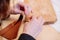 Detail shot of woman`s hands sewing a brown piece of leather with a needle