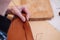 Detail shot of woman`s hands sewing a brown piece of leather with a needle