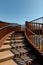 Detail of a stairway of a modern rusty bridge, with a clear blue sky behind it. Strong contrast between lights and shadows