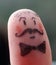 Detail of thumb finger painted with a funny man face