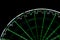 Detail view of an illuminated green and white ferris wheel and cabins in black night