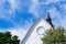 Detail view of a whitewashed church building with steeple under a blue sky with white clouds and green trees below