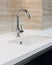 Detail of a white rectangular designer kitchen sink with chrome water tap against a tiled wall.