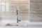 Detail of a white rectangular designer kitchen sink with chrome water tap against a tiled wall.