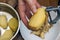 Detail of woman hands peeling fresh yellow potato with kitchen p