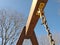 Detail of wooden frame swing set with metal ropes with blue sky background and leafless trees. Closeup of wooden swing for kids on