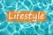 Detail of word `Lifestyle` on swimming pool water and sun reflecting on the surface