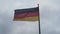 Detailed view of German national flag on pole waving in wind against cloudy background. Colour stripes on symbol. Berlin