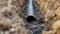 A detailed view of a pipe partially buried in the dirt. This image can be used to depict construction, plumbing, or infrastructure