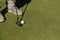 Details of the feet of a male golfer playing about to swing the ball on the green grass