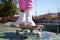 Details of a girl`s feet on a skateboard. The girl is wearing pink trousers and white boots. It is a sunny day