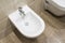 Details of white ceramic bidet with a running water in modern bathroom.