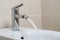 Details of white ceramic bidet with water running from tap in modern bathroom with beige tiles background. Close up