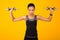 Determined Black Girl Exercising With Dumbbells Standing Over Yellow Background