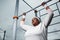 Determined overweight African woman practicing pull-up exercise outdoors