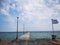 The developing flag of Greece on the background of the Mediterranean Sea. View from the pier to the water