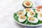 Deviled eggs stuffed with avocado, egg yolk and mayonnaise filling, garnished with bacon, on spinach leaves, horizontal copy space