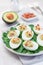 Deviled eggs stuffed with avocado, egg yolk and mayonnaise filling, garnished with bacon on spinach leaves, vertical
