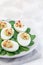 Deviled eggs stuffed with avocado, egg yolk and mayonnaise filling, garnished with bacon, on spinach leaves, vertical copy space