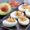 Deviled eggs stuffed with avocado, egg yolk and mayonnaise filling, garnished with bacon, square format