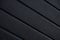 Diagonal close-up of black striped corrugated surface with uneven texture