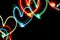 Diagonal row of multicolored neon glowing hearts on black background with copy space