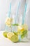 Diagonal top view of three bottles with blue straw, water and slices of lemon, lime and mint, on white table with half lemons