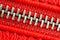 Diagonal zipper tightly closed binding together two layers of red fabric textile and red leather under high magnification detail