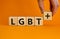 Dice form the acronyms `LGBT+`. Male hand. Beautiful orange background. Concept, copy space