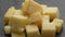 Diced cheese rotates on a black plate, close up. Dairy products concept