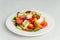 Diced greek village horiatiki salad served on white plate. Horizontal, side view, closeup