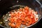 DICED TOMATOES AND ONIONS BEING COOKED IN FRYING PAN ON OVEN.