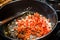 DICED TOMATOES AND ONIONS BEING COOKED IN FRYING PAN ON OVEN.