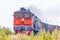 A diesel locomotive pulls a train of freight cars across the fields. Front view