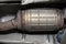 A diesel particulate filter in the exhaust system in a car on a lift in a car workshop, seen from below.