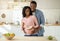 Diet for healthy pregnancy. Positive black guy hugging his lovely expectant wife with balanced meal in kitchen