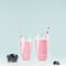 Diet milk beverages in elegant glass with blueberries in bowl, striped straws on pastel soft light blue background, square.