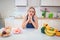 Diet struggle. Young sad woman in blue T-shirt choosing between fresh fruit vegetables or sweets in the kitchen. Choice