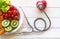 Diet and weight loss for healthy care with medical stethoscope, with red heart and fresh vegetable salad and healthy food on woode