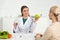 Dietitian in white coat holding apple and glass of water and patient at table