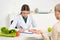 Dietitian in white coat writing in clipboard and patient at table