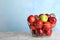 Different apple among red ones in metal basket on table.